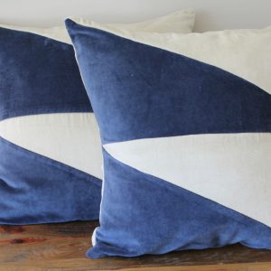 A pair of velvet cushions with blue and white triangular pattern and gold striped detailing are arranged on a wooden surface.